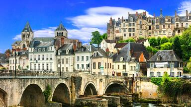 Une ville historique, avec un pont de pierre, un clocher d’église imposant et un château qui se profile à l’arrière-plan.