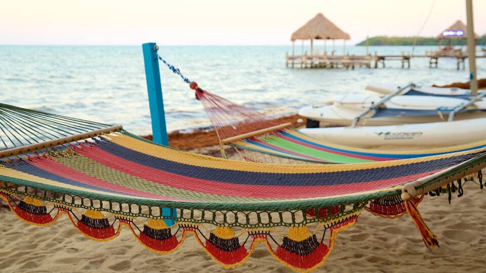 A colorful hammock on a beach with boats and a pier in the background.