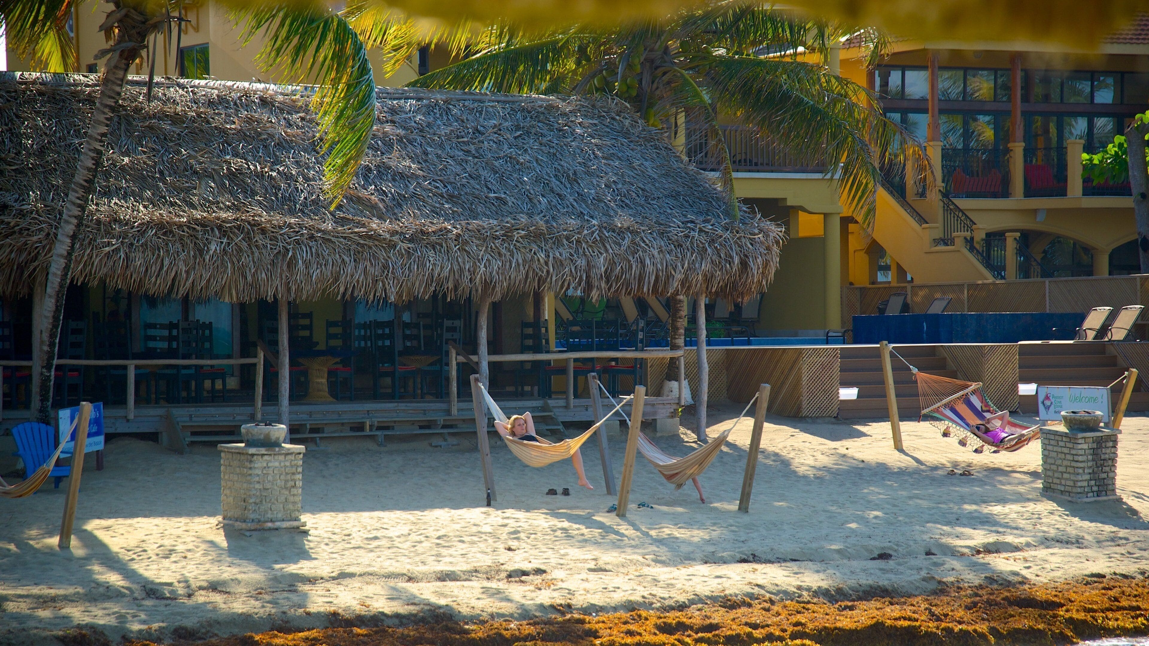 Una playa con cabañas de techo de paja, hamacas y un edificio de fachada amarilla.