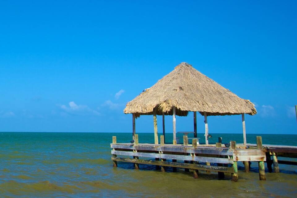 A thatched-roof hut on a wooden pier extending into turquoise waters.
