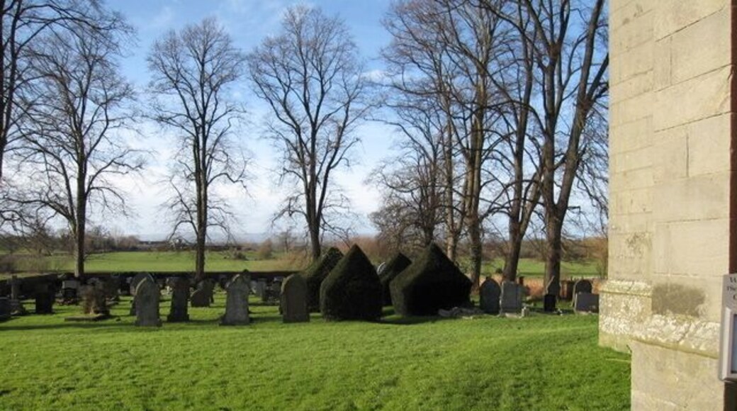 St Deiniol's, Worthenbury - graveyard. A short avenue of clipped yews flanks the path through the graveyard. On the right hand side of the photo is a benchmark by the door to the church - see 1129475.