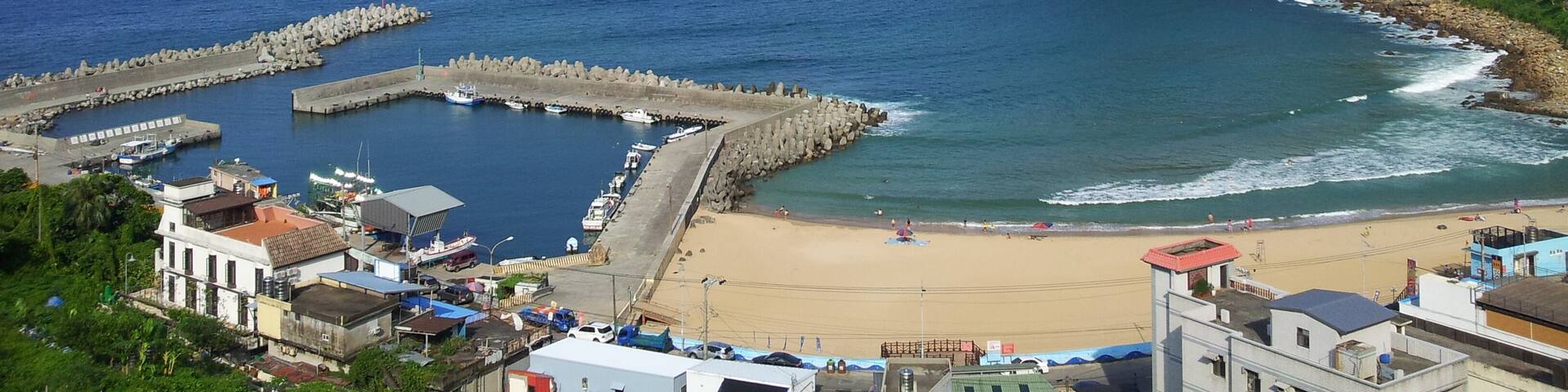 A coastal town with a beach, rocky breakwaters, and a distant island.