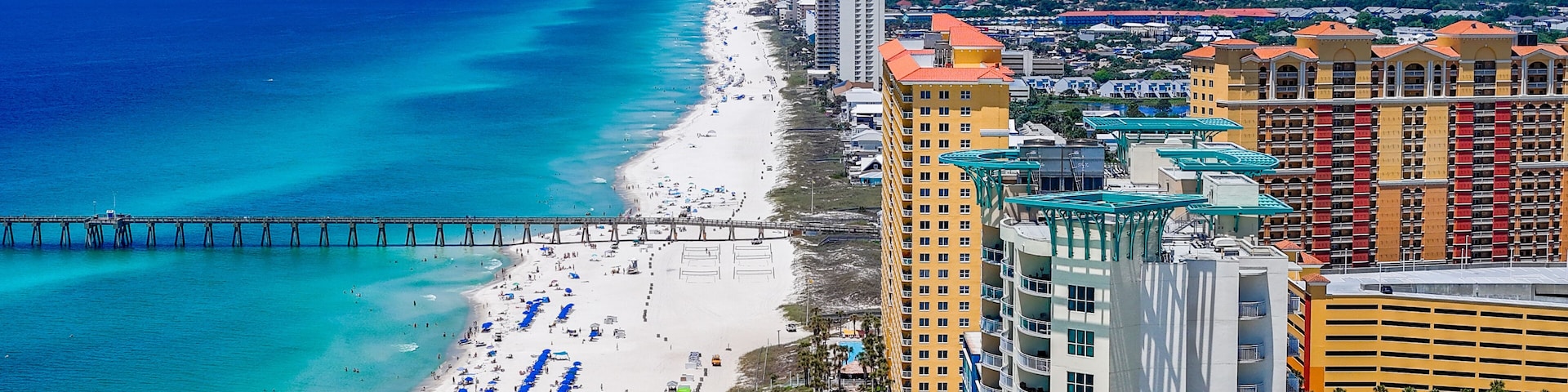Paisagem costeira com praia, um cais e edifícios altos.