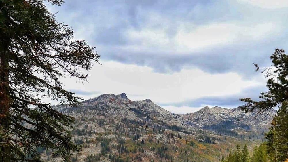 Ein Wanderer auf einem felsigen Pfad, umgeben von herbstlich gefärbten Bäumen und Bergen im Hintergrund.