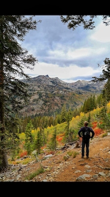 A hiker on a rocky trail surrounded by autumn-colored trees and mountains in the background.