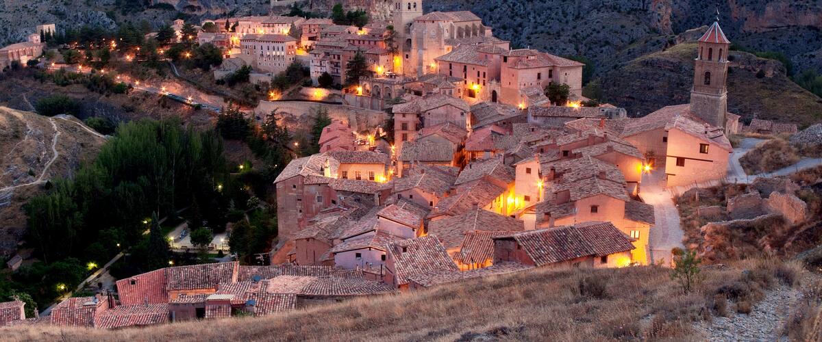 A historic town nestled in a mountainous area with illuminated buildings and a prominent church tower.
