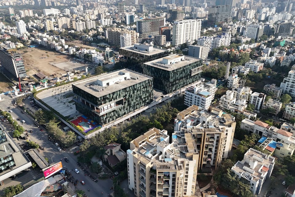 An aerial view of a densely populated urban area with high-rise buildings, a large open plaza, and a busy road with vehicles.