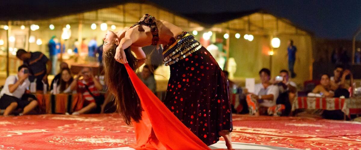 A couple performing a dance on a patterned carpet in front of a tented area with people seated at tables.