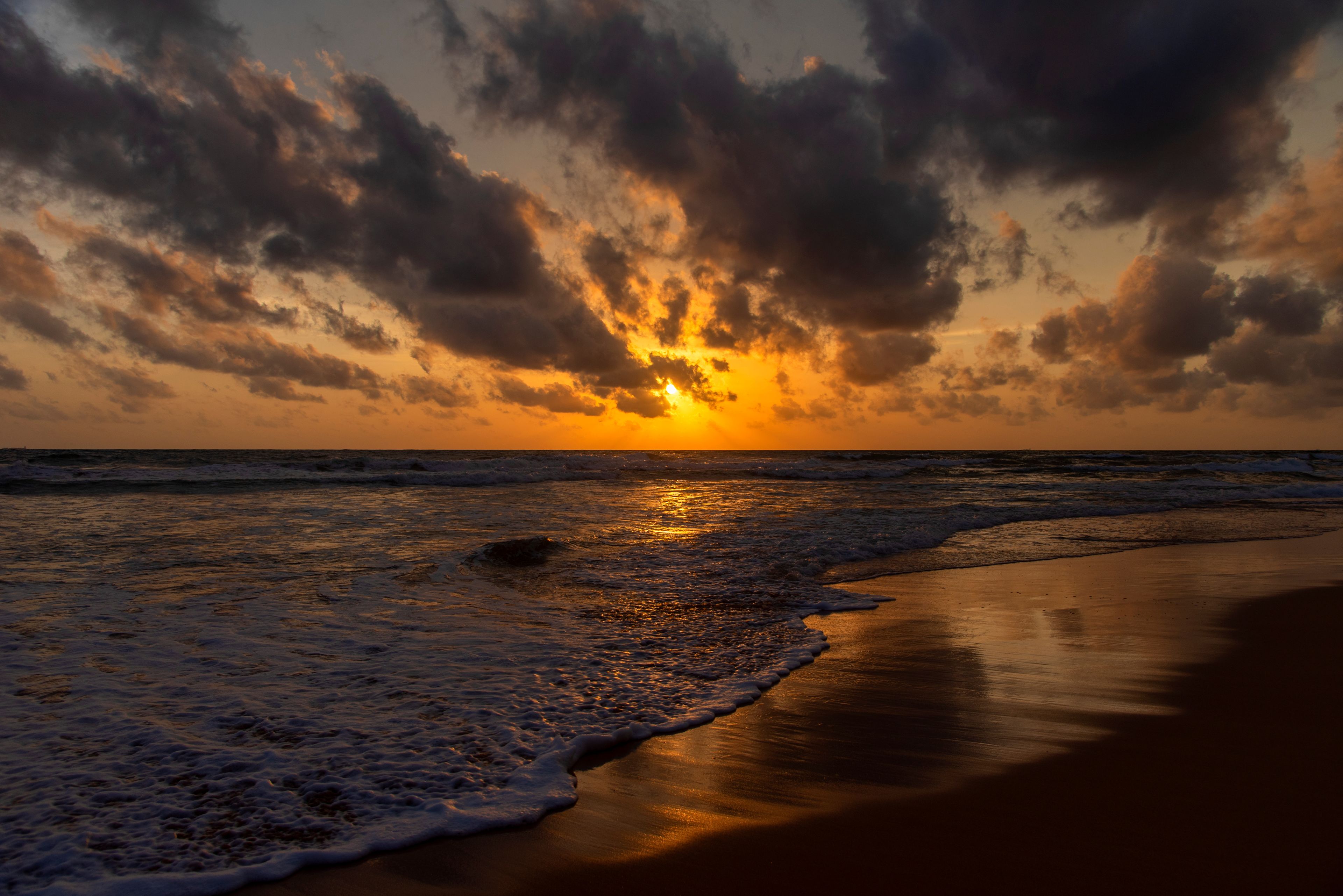 A sunset over a beach with waves and a cloudy sky.