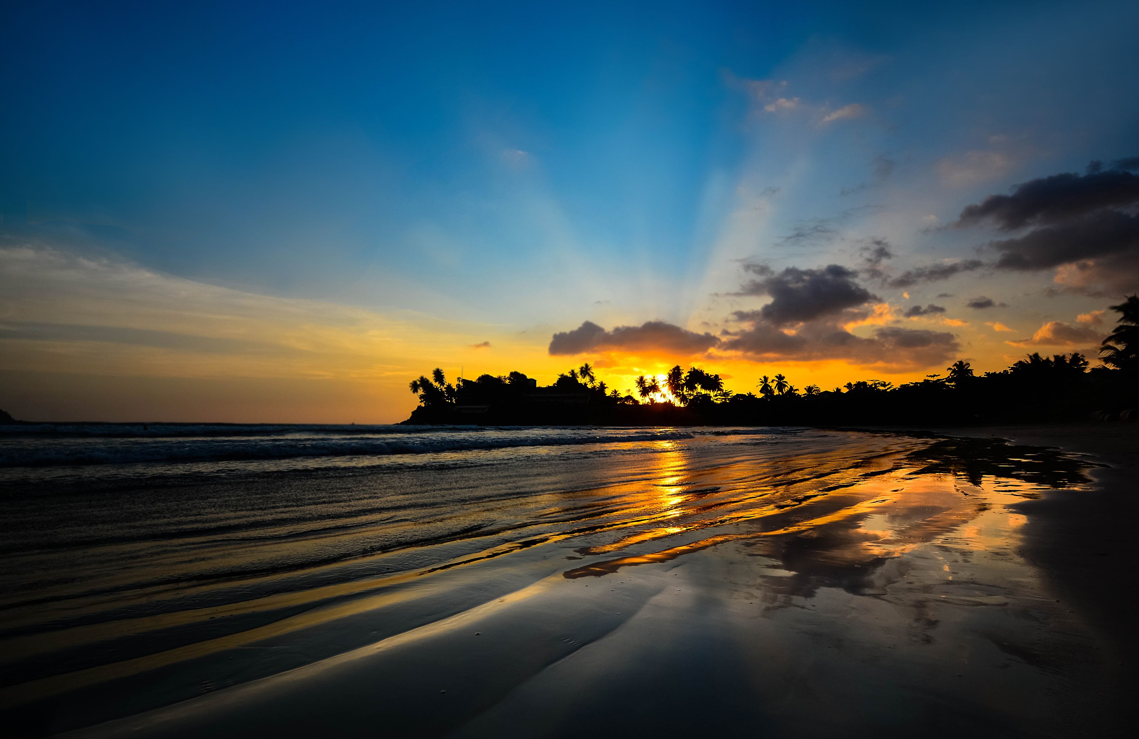 A beach at sunset with the sun setting over the horizon, casting a golden glow on the wet sand.