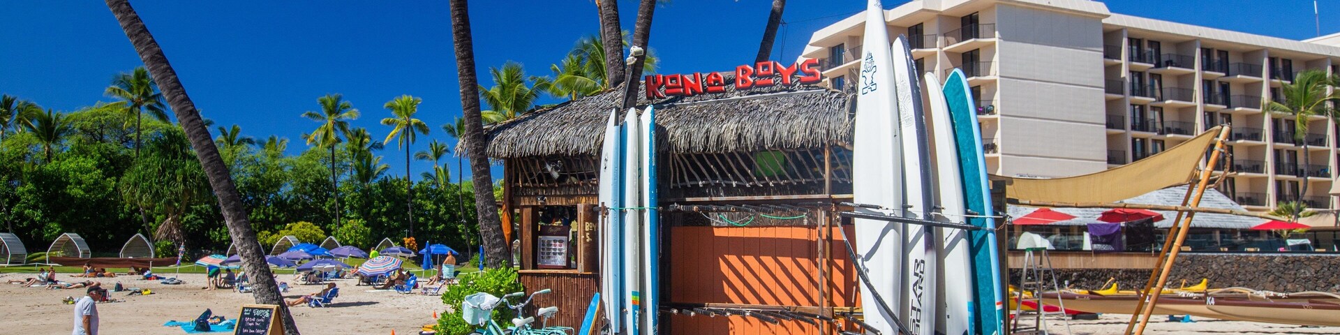 Un restaurante frente al mar llamado 'Kona Boys', con tablas de surf y bicicletas.