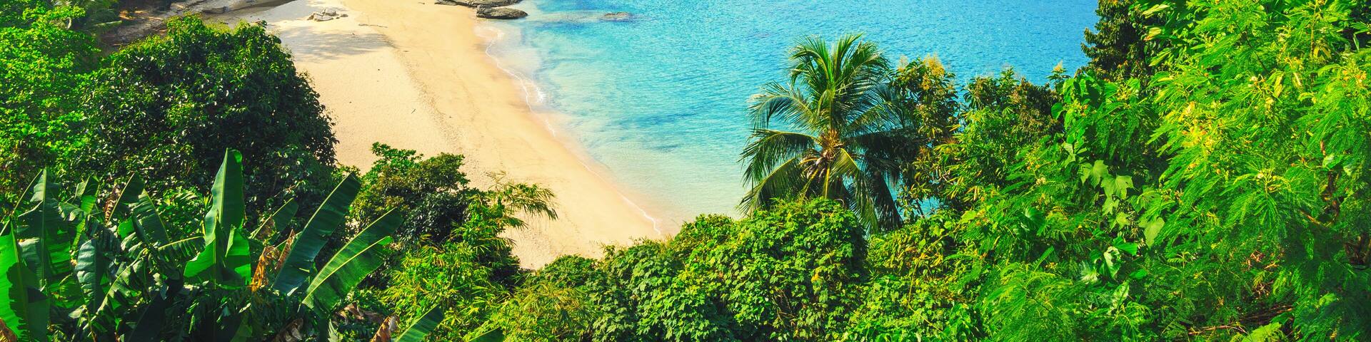 Una playa tropical con aguas turquesas cristalinas, exuberante vegetación y montañas al fondo.