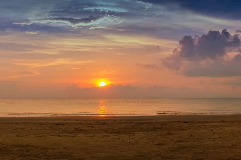 A beach with a sunset, ocean, and a distant island.