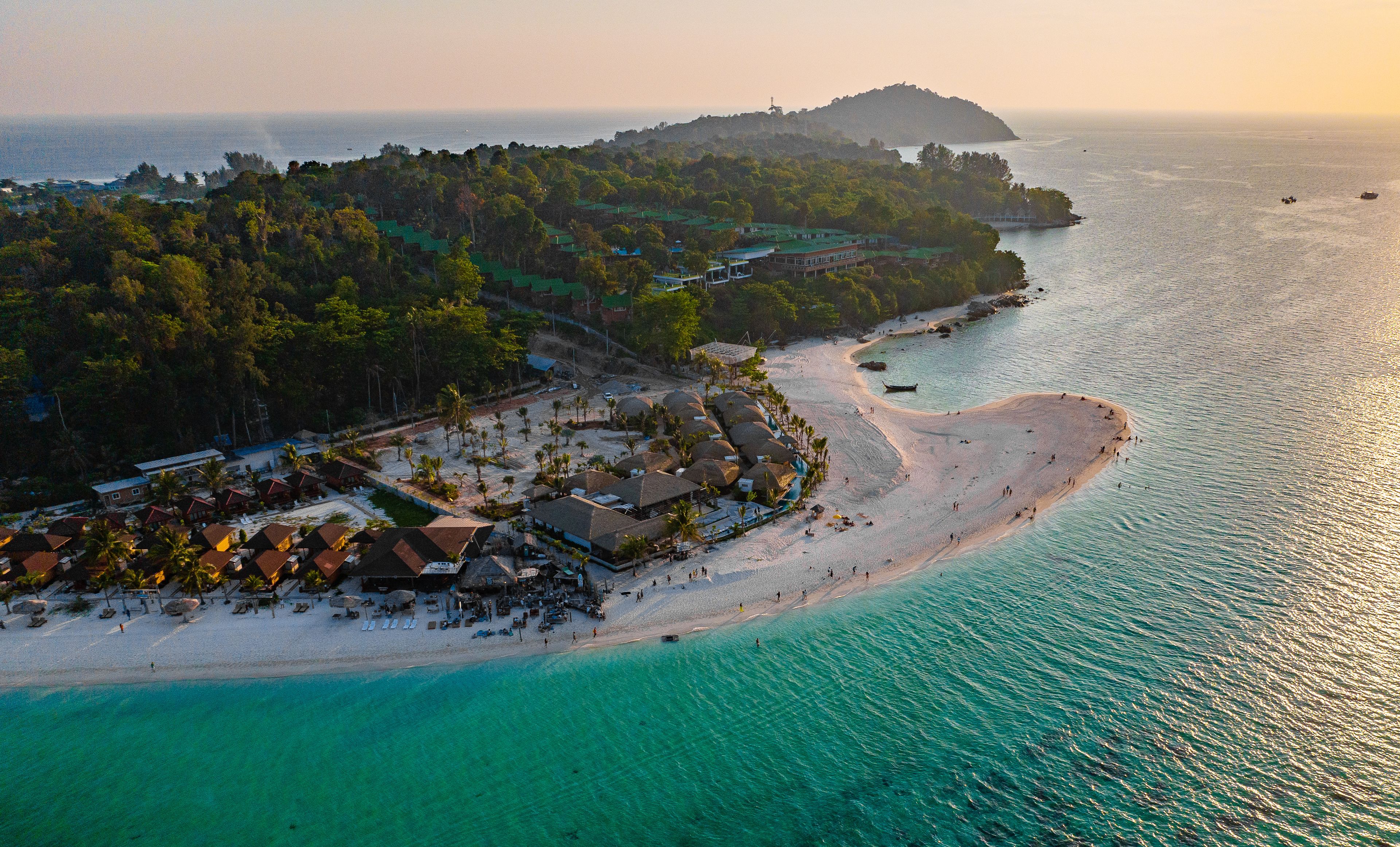 Um resort costeiro com uma praia arenosa, águas turquesa cristalinas e uma ilha coberta por floresta ao fundo.