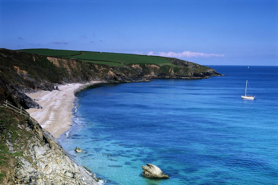 A coastal landscape with a sandy beach, green hills, and a clear blue sea.