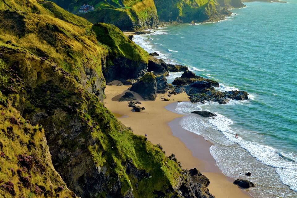 Un paysage côtier avec une plage de sable, des falaises rocheuses et une colline herbeuse.