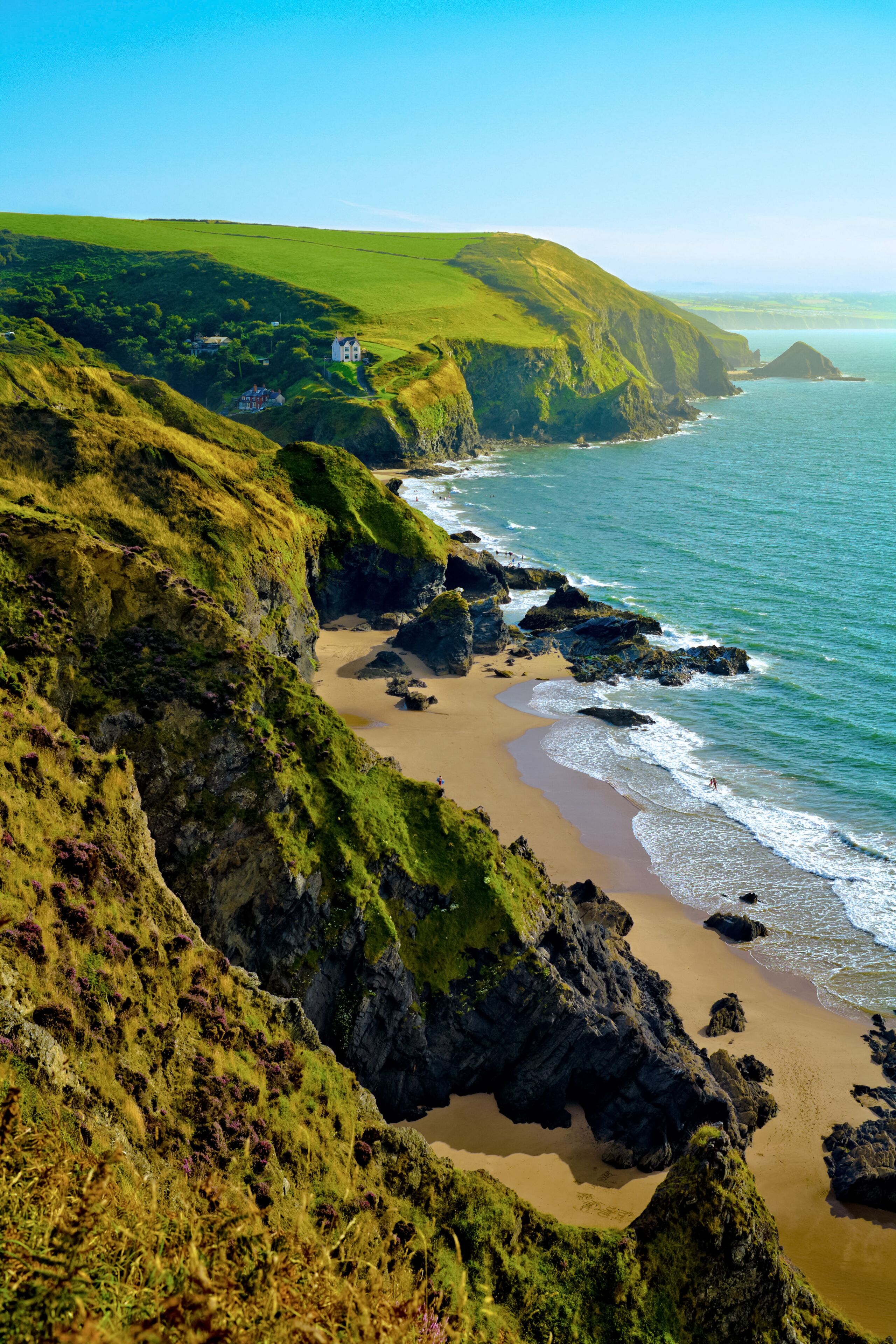 A coastal landscape with a sandy beach, rocky cliffs, and a grassy hill.