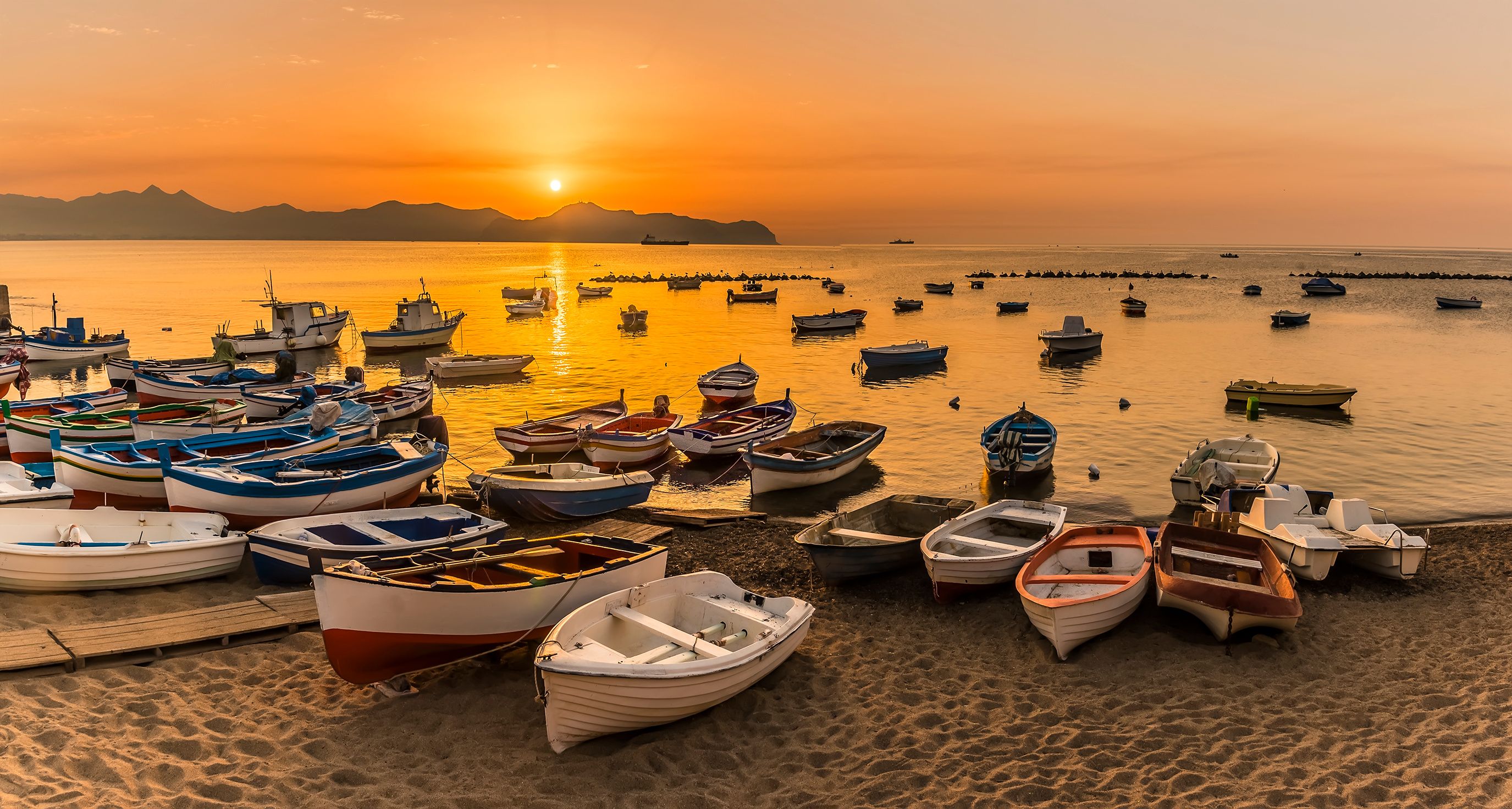 A panorama view of colourful fishing boats at Aspra Sicily as the sun sets over the Gulf of Palermo on a summer's evening