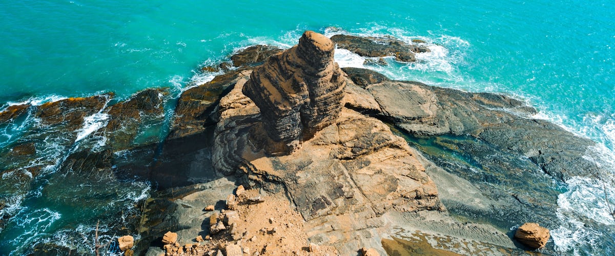 A rocky coastline with clear turquoise waters and a prominent rock formation.