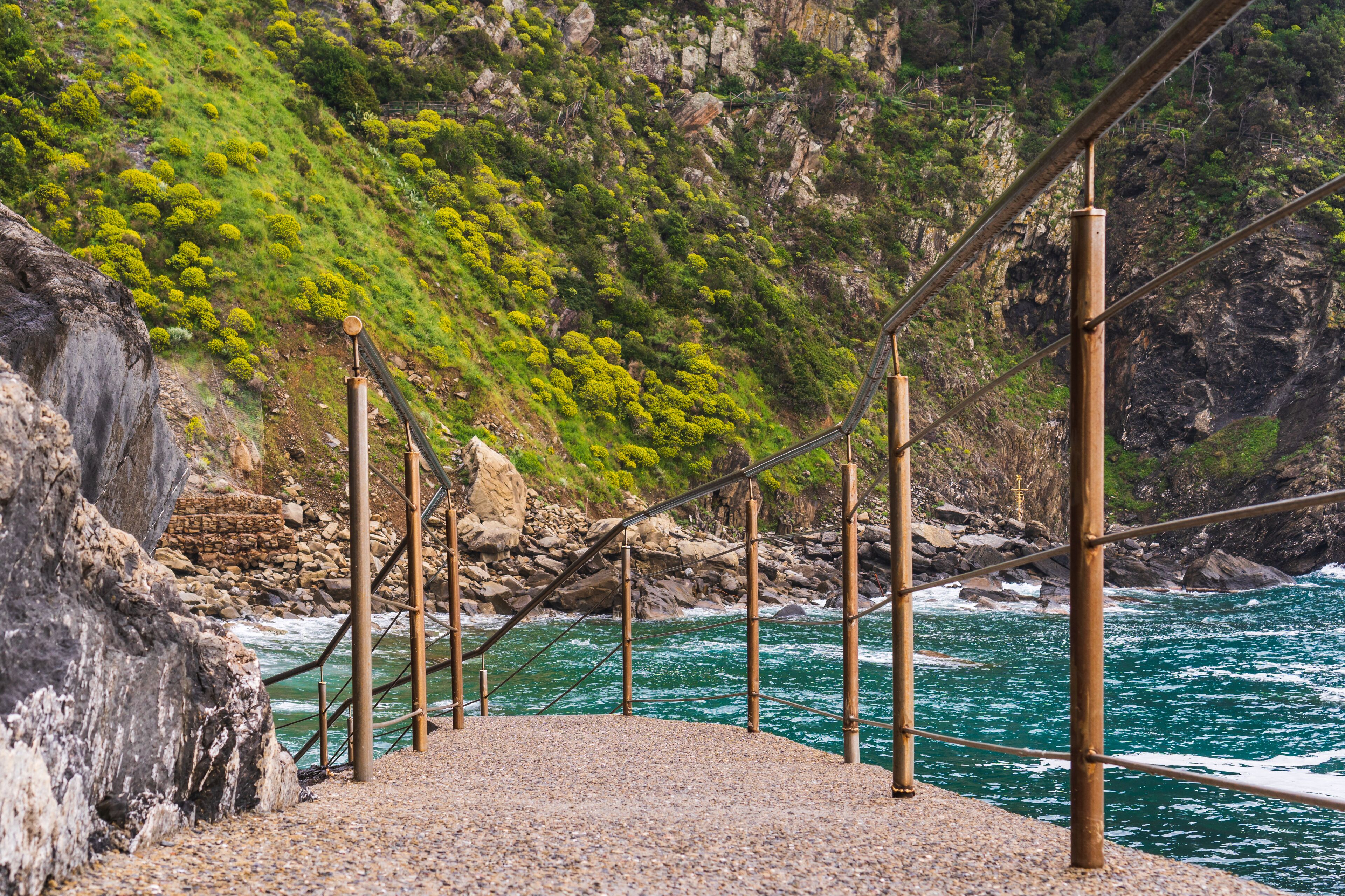 Narrow path with metal handrails leading down to the lovely and rocky Riomaggiore Beach (Spiaggia del Paese) in Cinque Terre, Italy.