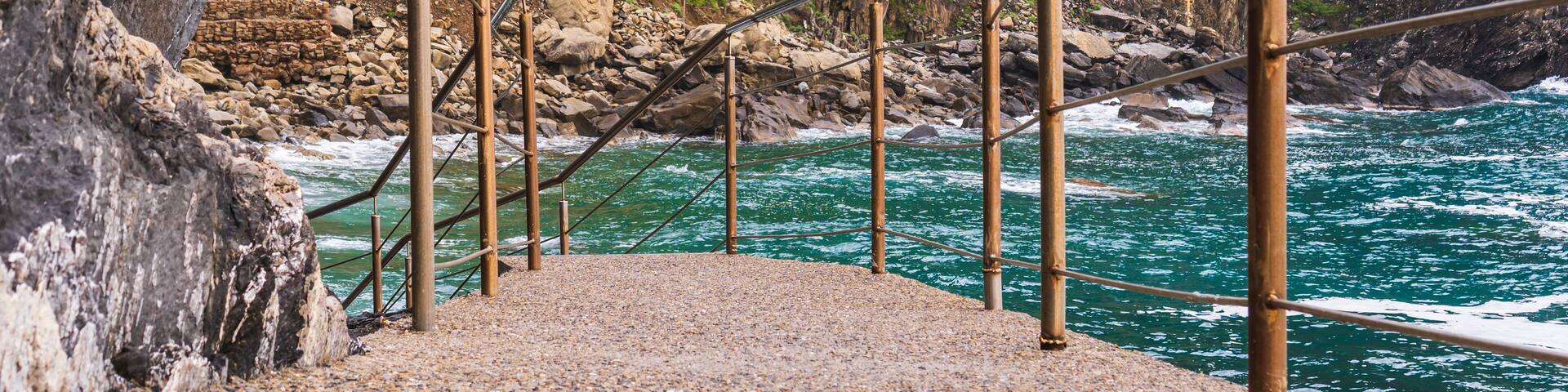 Un puente colgante sobre una costa rocosa con una ladera verde al fondo.