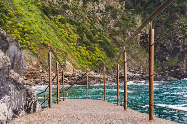 Narrow path with metal handrails leading down to the lovely and rocky Riomaggiore Beach (Spiaggia del Paese) in Cinque Terre, Italy.
