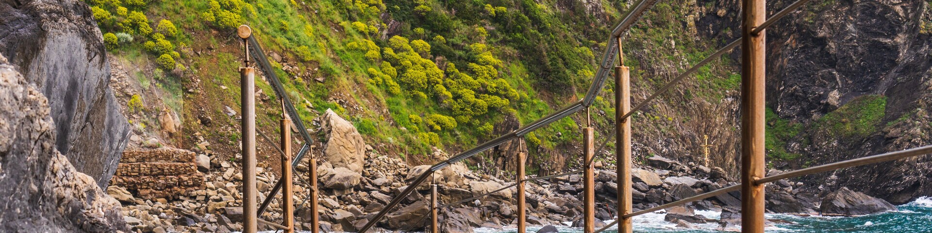 Narrow path with metal handrails leading down to the lovely and rocky Riomaggiore Beach (Spiaggia del Paese) in Cinque Terre, Italy.