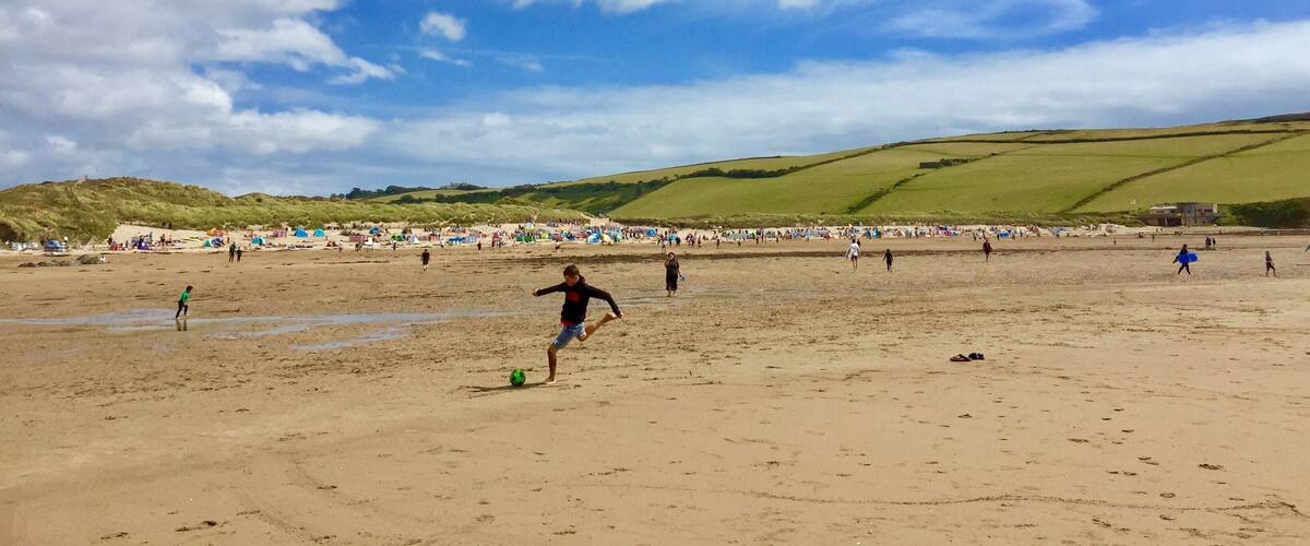 A beach with people playing soccer, tents, and hills in the background.