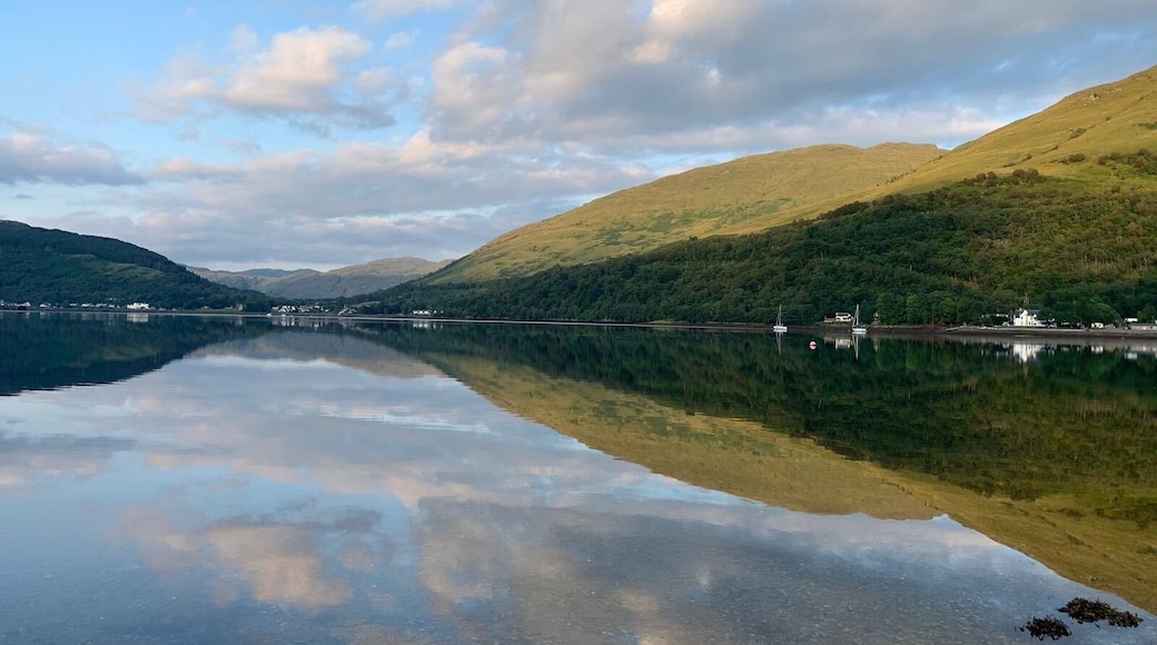 Beautiful view of Loch Long in Ardgartan, Scotland .
Clear blue water filled with pebbles and the reflection of the mountains and hills .