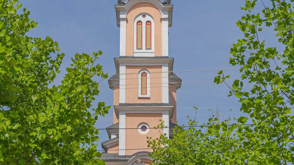 A church with a tall bell tower and a cross on top, surrounded by trees.