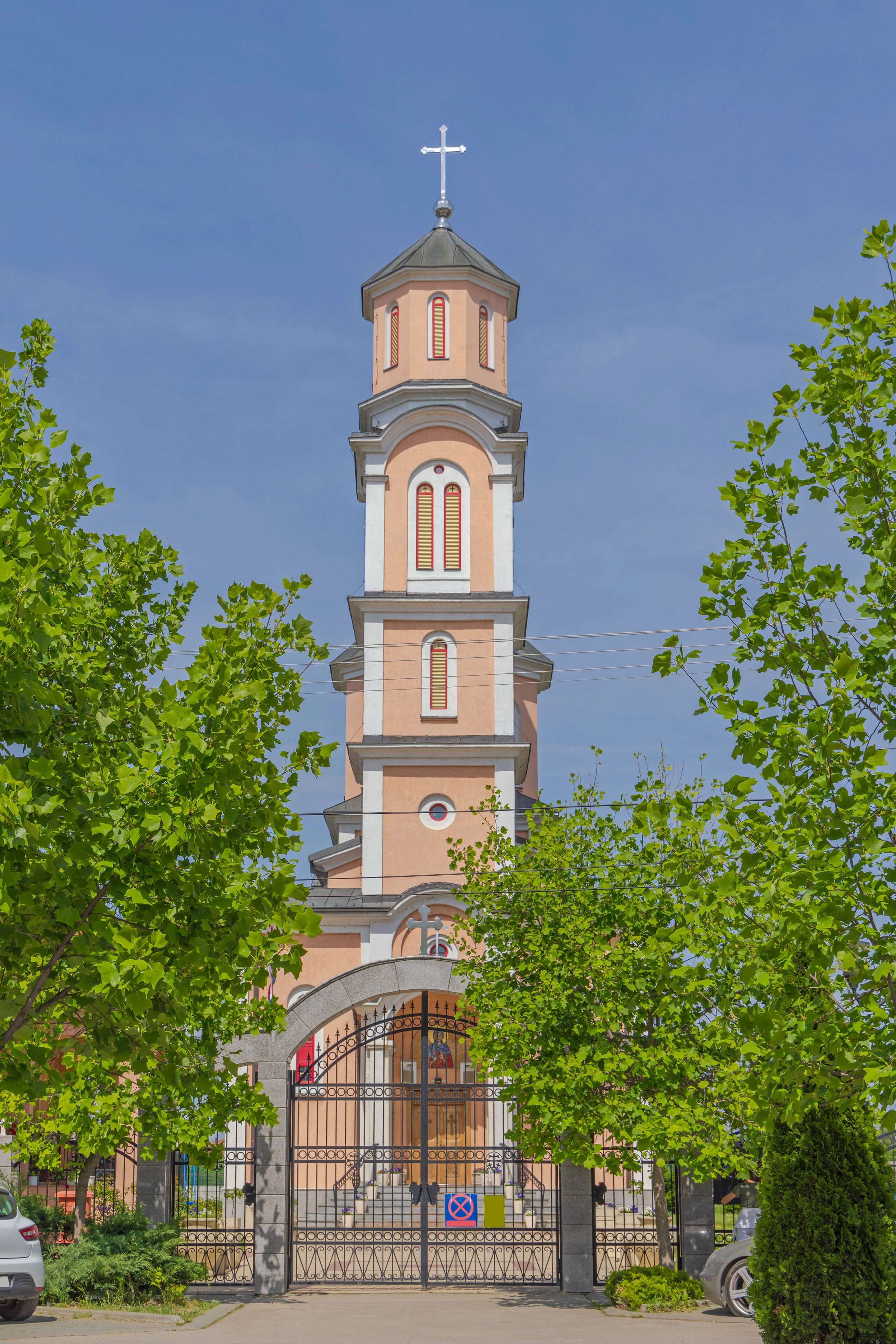 A church with a tall bell tower and a cross on top, surrounded by trees.