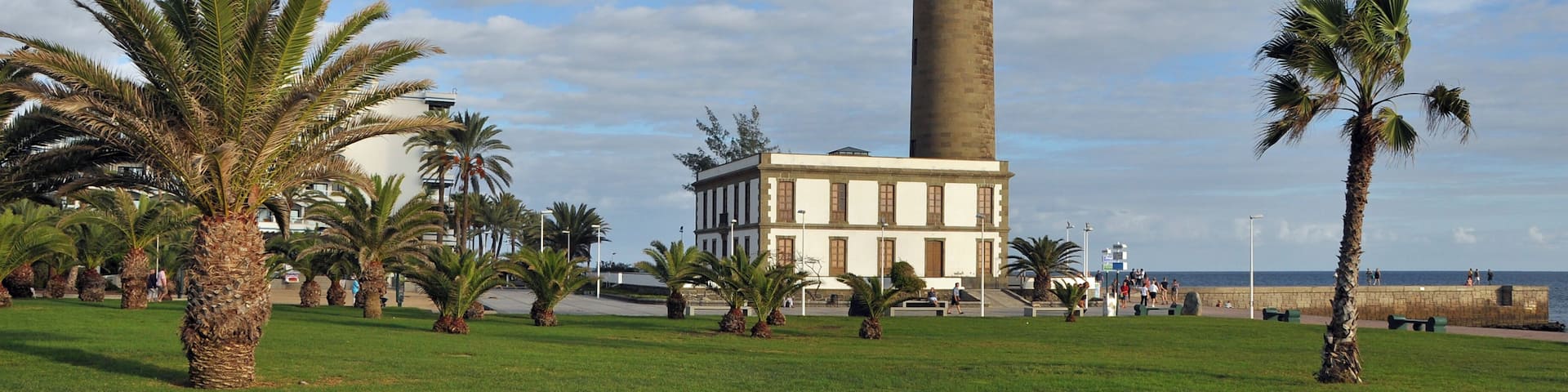 A tall tower with a lighthouse, surrounded by palm trees and a building.