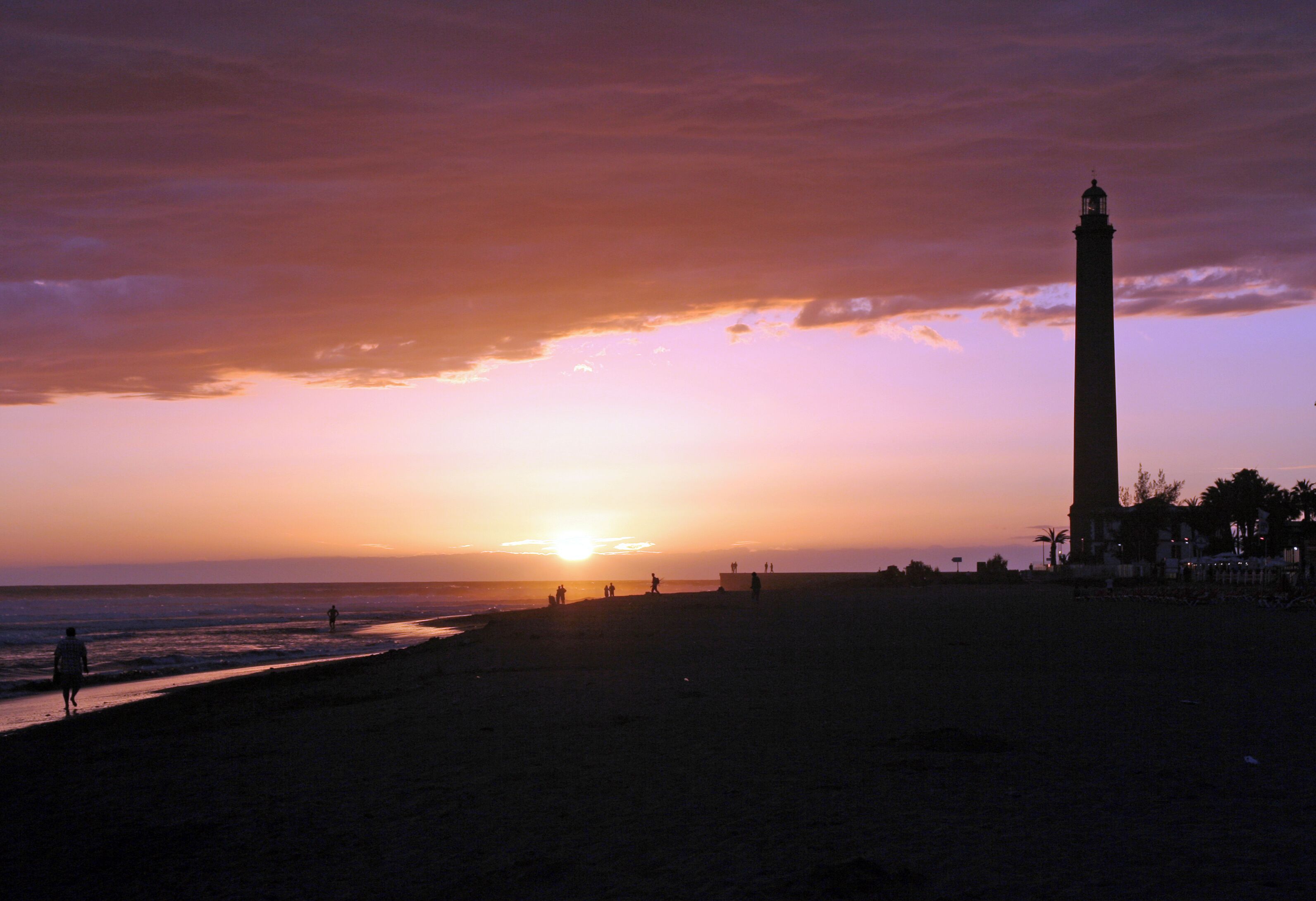 Una playa al atardecer con un faro al fondo.