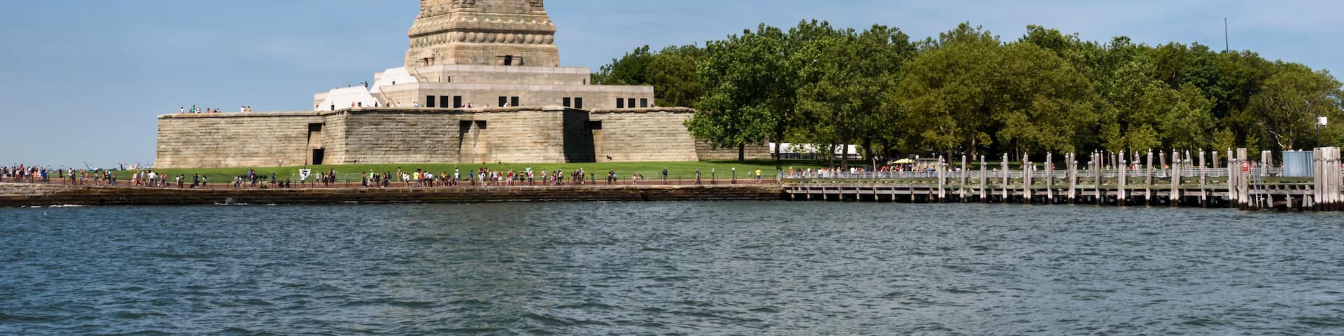 La statue de la Liberté, sur l’île de la Liberté, sous un ciel dégagé et avec une mer calme.