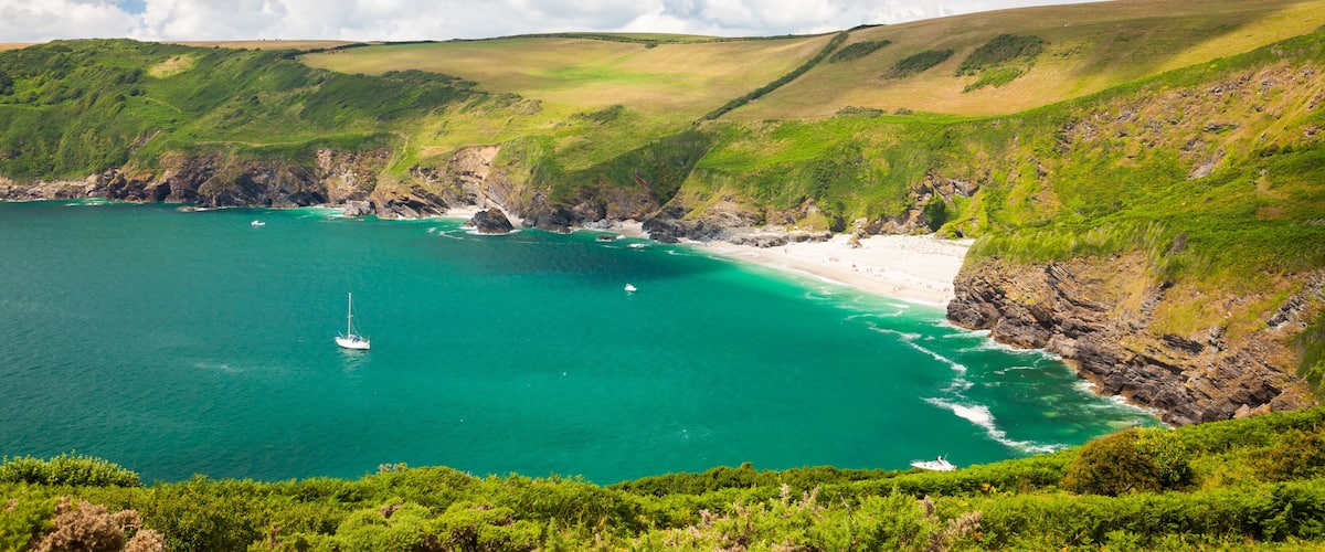 A coastal landscape with a clear blue sea, a sandy beach, and green hills.