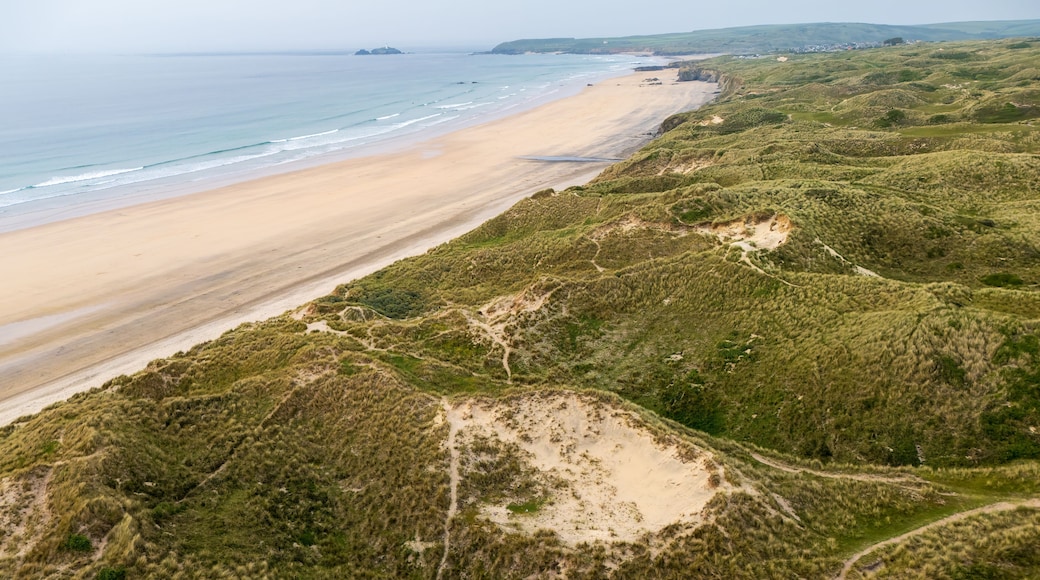 Paisaje costero con playa arenosa, dunas verdes y una vista distante del mar.