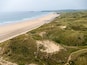 Aerial view of the vast sandy expanse of Upton Towans Beach bordered by rolling grassy sand dunes and the turquoise waters of the Atlantic Ocean at Gwithian, Cornwall, United Kingdom.