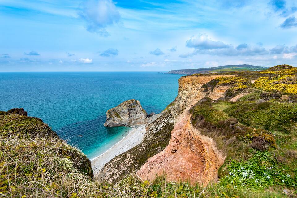 A coastal landscape with a rocky cliff, beach, and ocean.