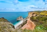 Un paysage côtier avec une falaise rocheuse, une plage et l’océan.