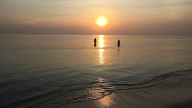 A sunset over a calm sea with two people standing in the water.