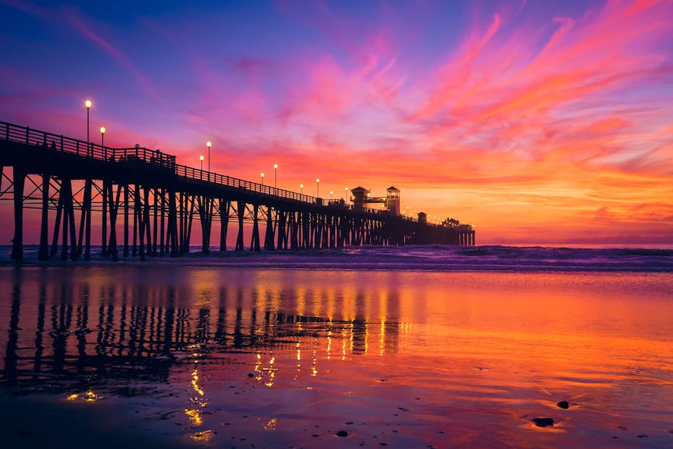 A pier with lights reflecting on the water at sunset.