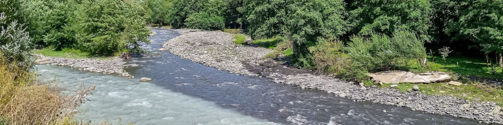 Un río serpentea a través de un paisaje montañoso, con abundante vegetación y riberas rocosas.