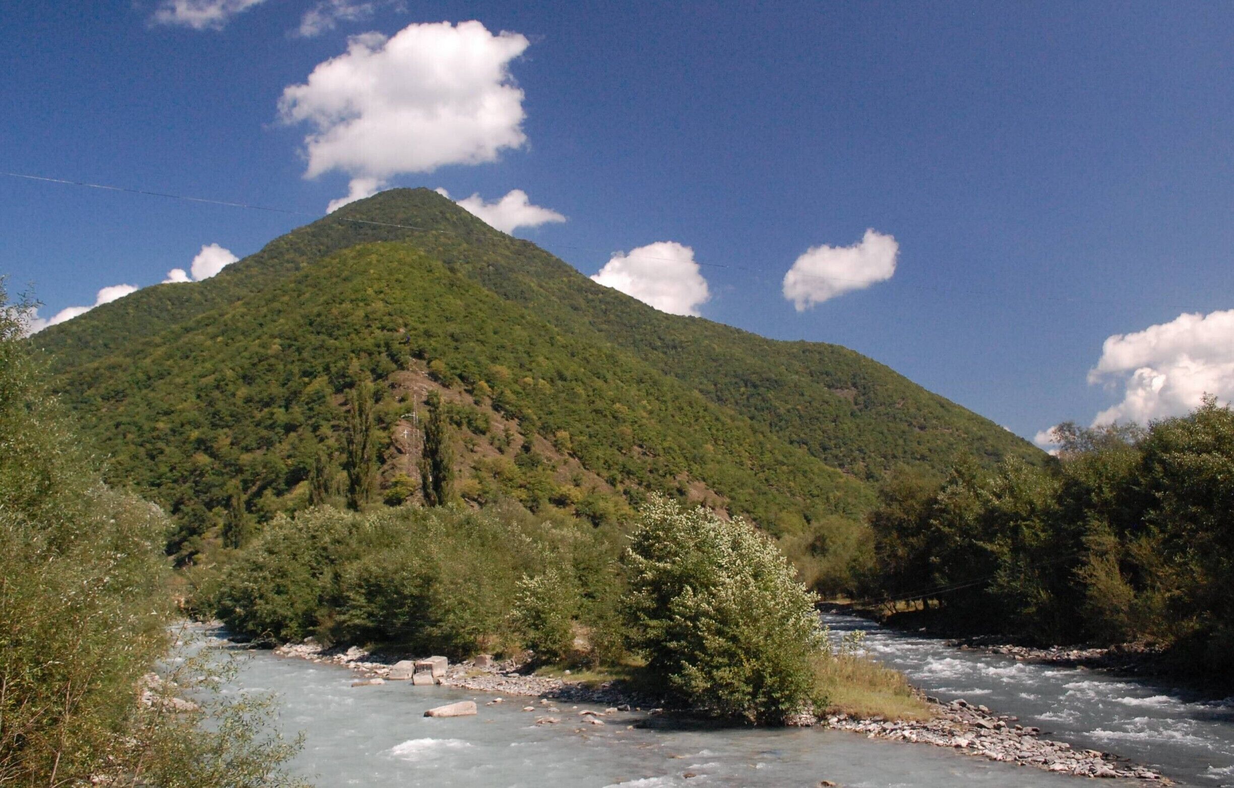A river flowing through a valley with a mountain in the background.