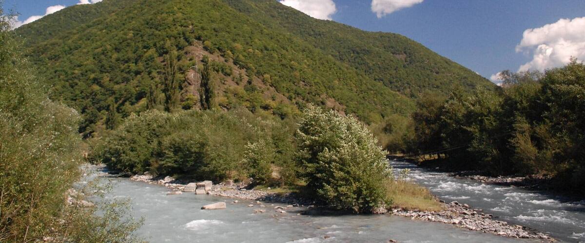 A river flowing through a valley with a mountain in the background.