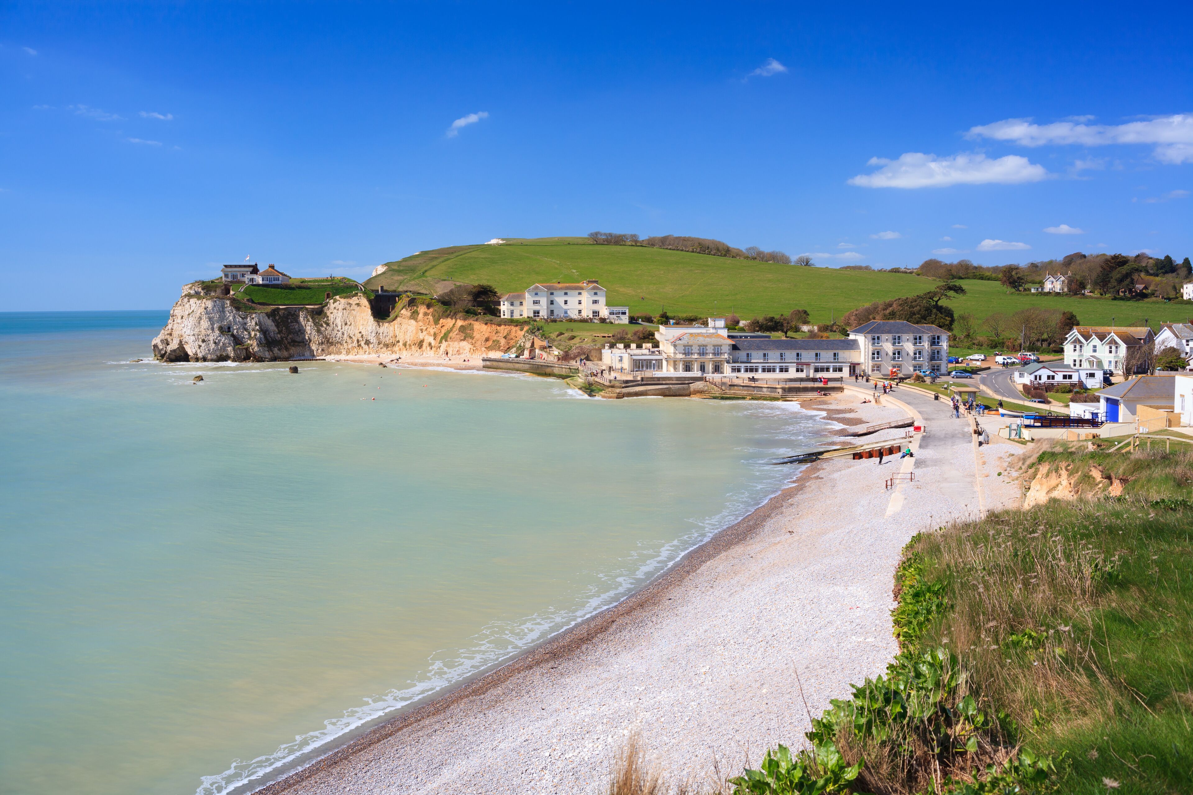 A coastal town with a sandy beach, houses, and a cliff overlooking the sea.