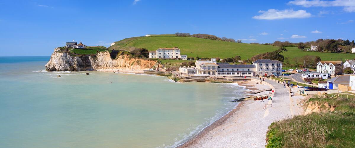 A coastal town with a sandy beach, houses, and a cliff overlooking the sea.