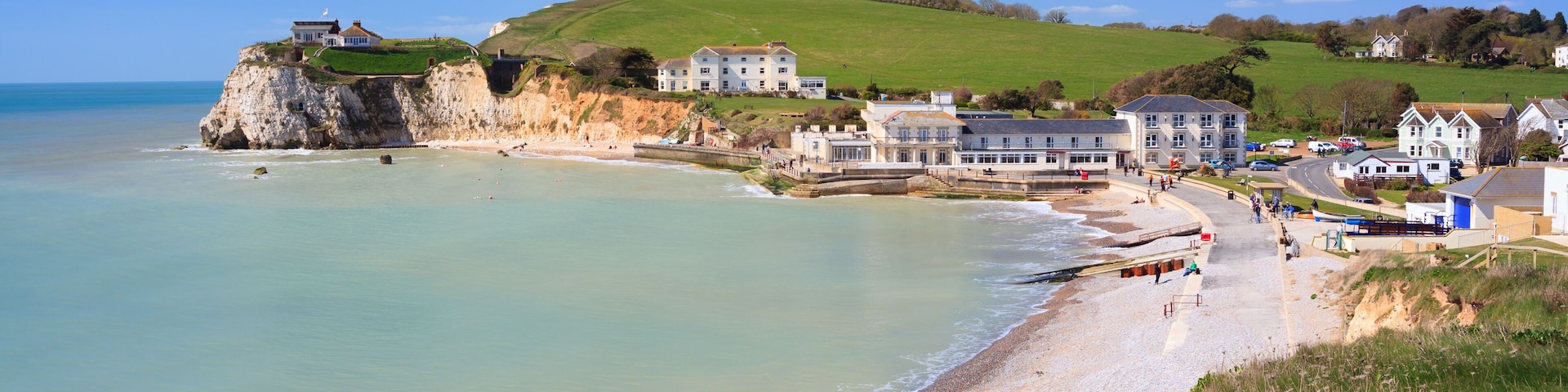 A coastal town with a sandy beach, houses, and a cliff overlooking the sea.