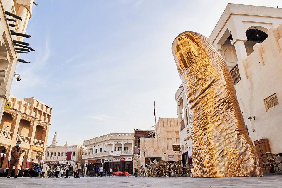 A square with a large golden statue, historic buildings, and a clear sky.