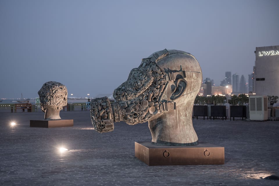 Eine Skulptur von Kopf und Oberkörper aus Metall, im Hintergrund eine Stadtansicht.