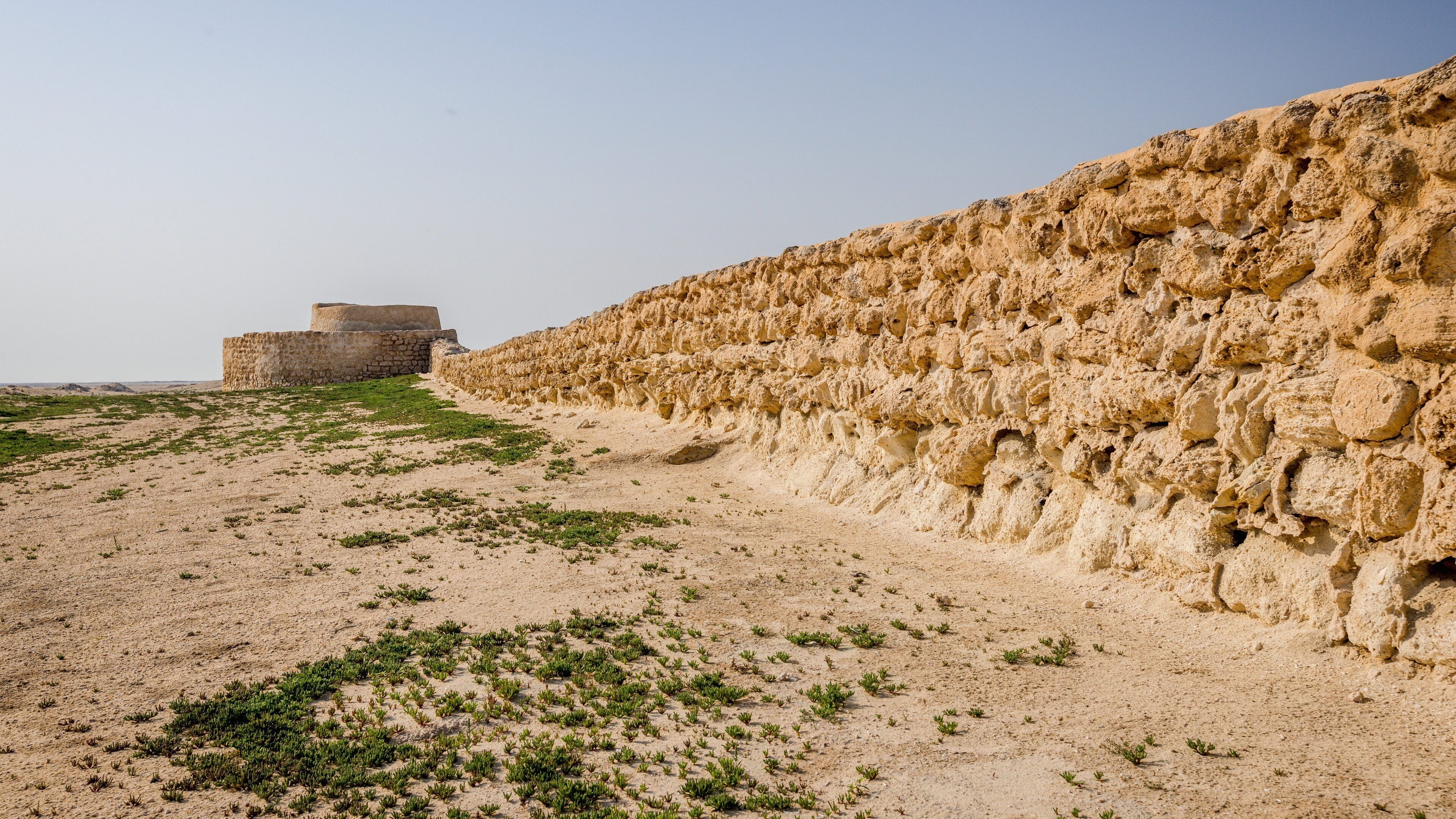 A desert landscape with a stone wall and a small building.